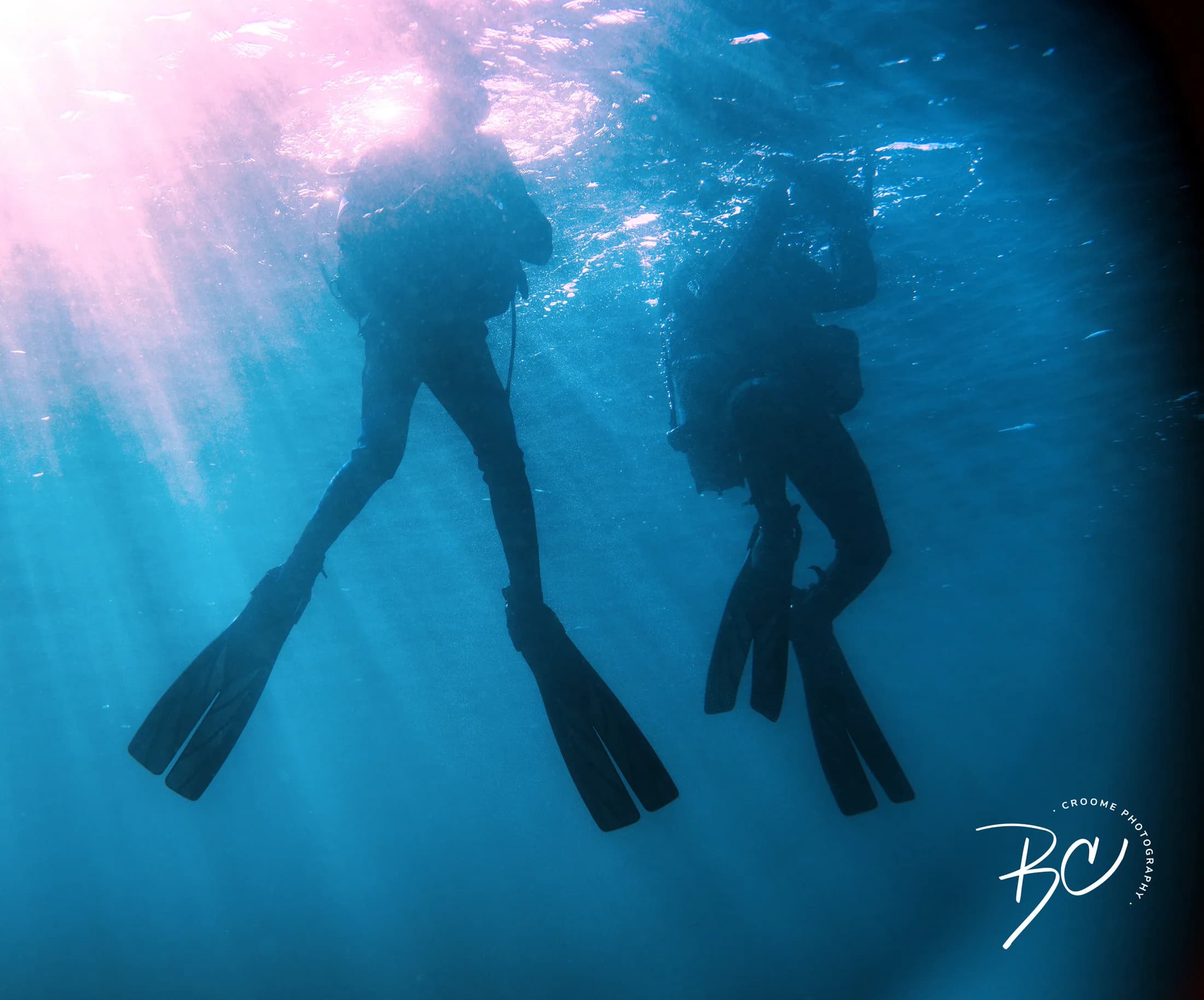 Divers descending through blue water by Croome Photography