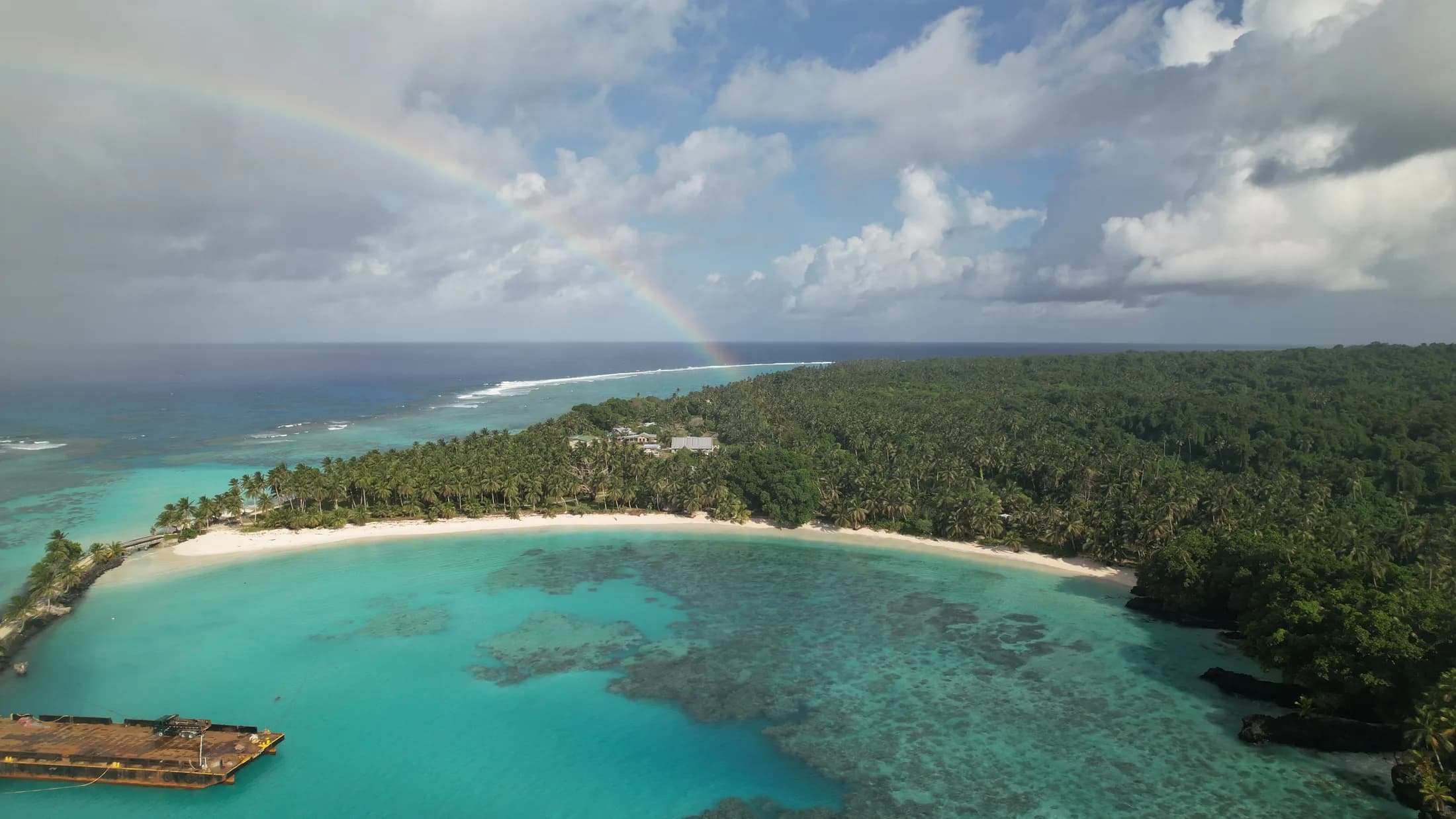 Aerial view of a rainbow arching over a reef island by Croome Photography